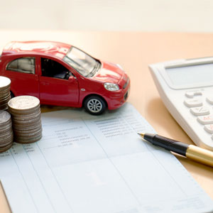 A car, insurance paper & calculator surrounded by coins on a desk.