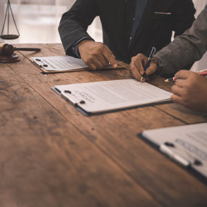 Two business people signing papers at a table representing personal injury - Mullins & Blake Attorneys