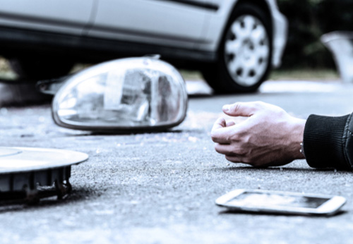 Car headlight and broken pieces on the road next to a hand and a phone, symbolizing a pedestrian accident in Bella Vista, AR