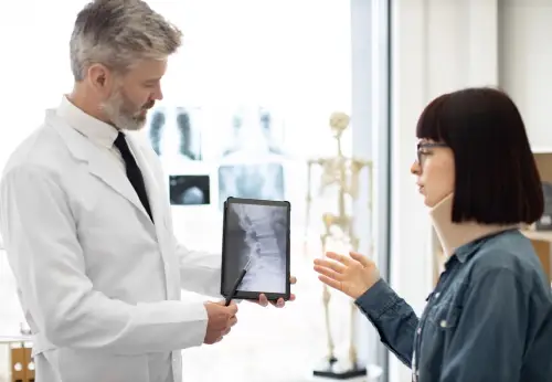 Doctor in a white coat showing a spinal X-ray on a tablet to a patient